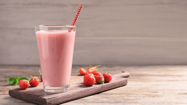 Strawberry milk in glass with straw on cutting board with strawberries