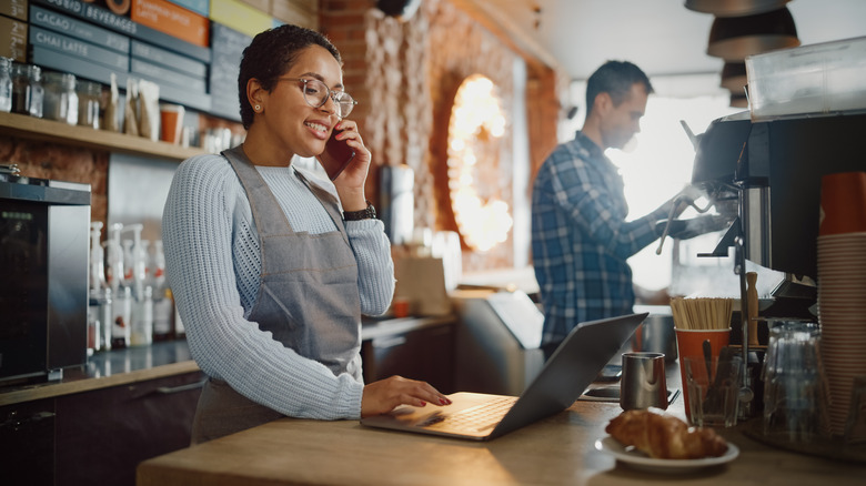 woman working at coffee shop looking at laptop while on phone