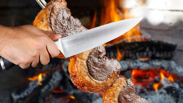 Slicing steak on skewer at brazilian steakhouse