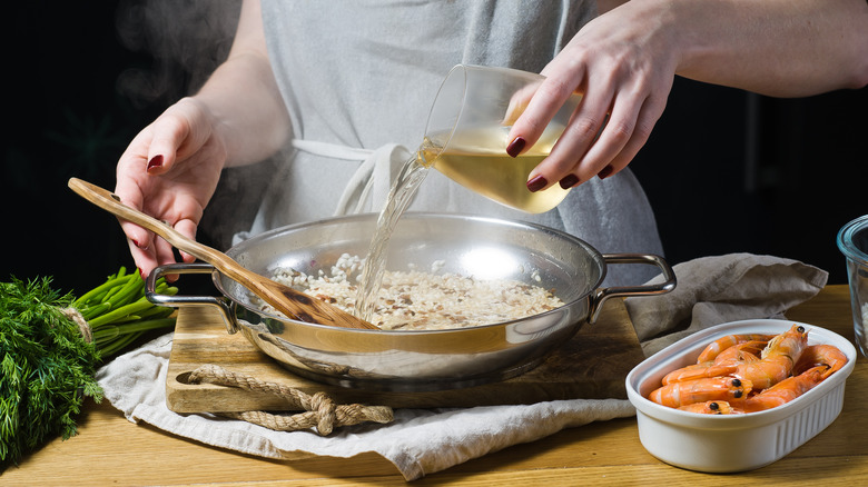 Chef pours white wine into a risotto