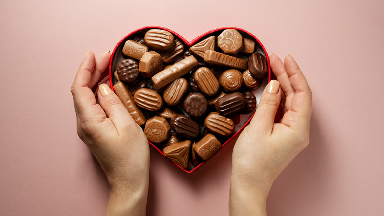 Hands holding a heart-shaped box of chocolates