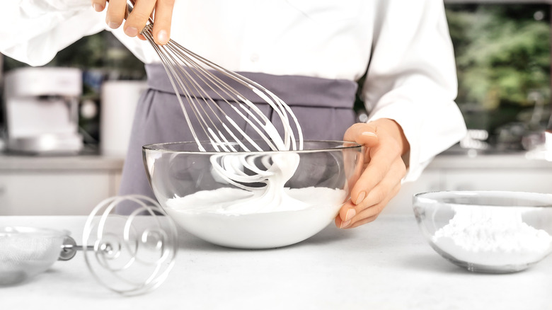 Woman whisking egg whites by hand in a glass bowl