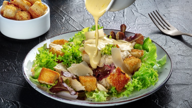 dressing drizzling onto Caesar salad