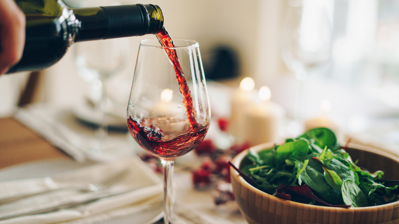 Pouring red wine into glass beside bowl of spinach