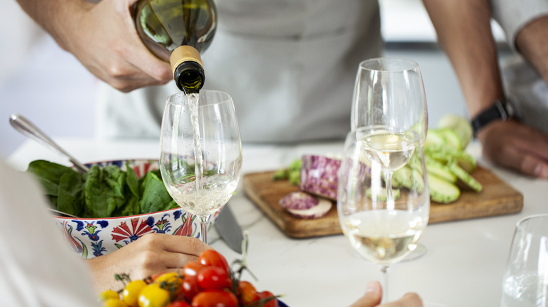 Pouring white wine into glass beside chopped veggies