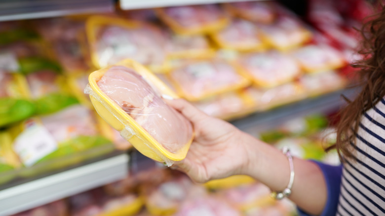 person holding chicken in grocery store package