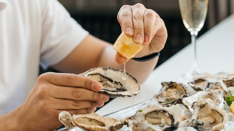 Person squeezing lemon on oyster