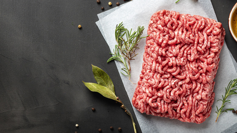 Ground beef on black background with green herbs