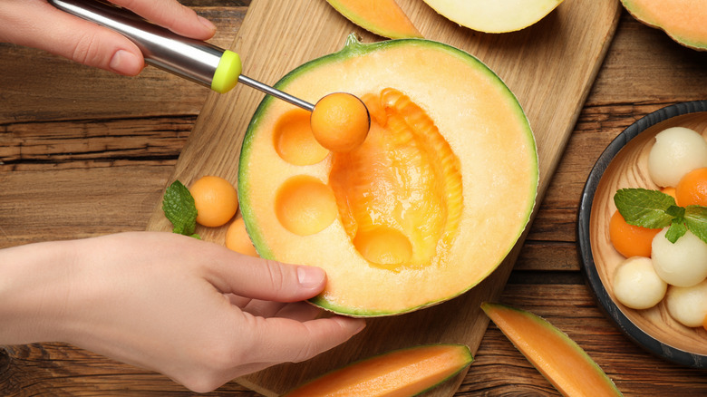 person preparing cantaloupe with melon baller