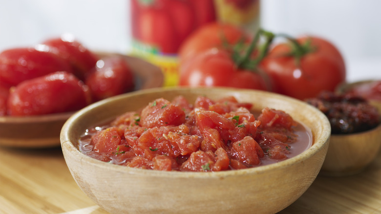 stewed tomatoes in a bowl with fresh tomatoes in background