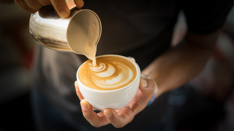 A man pours milk into a coffee mug