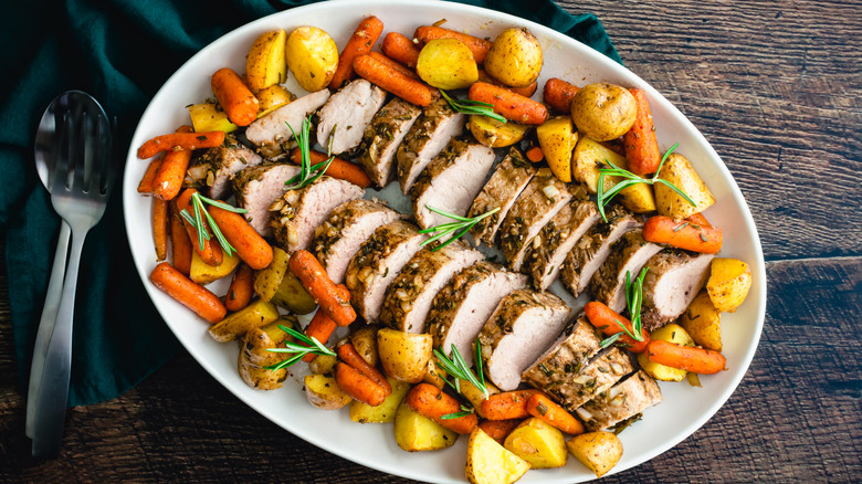 White platter of roast pork tenderloin medallions surrounded by vegetables