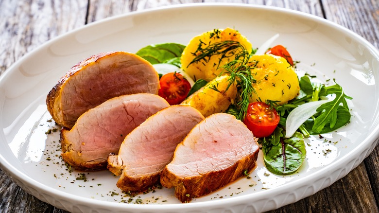 Slices of medium-rare pork tenderloin on white plate with vegetables