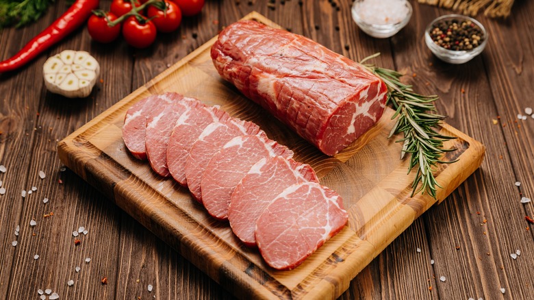 Fresh raw pork loin piece and slices on cutting board with aromatics and vegetables