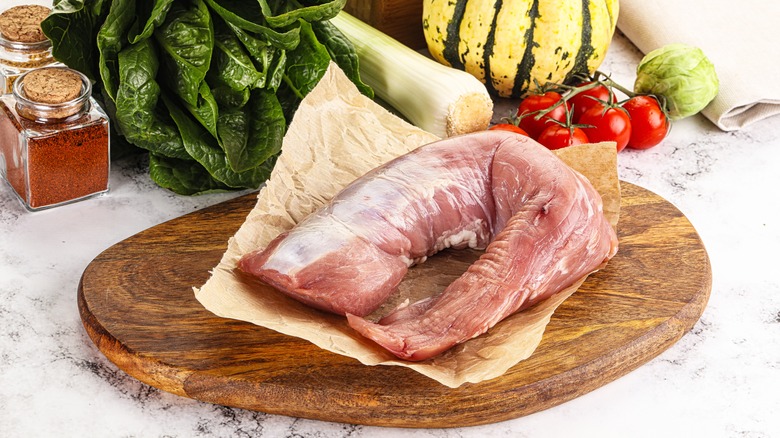 Raw pork tenderloin on cutting board with spices and vegetables