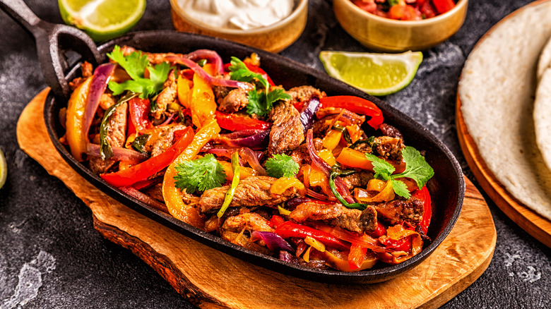 A cast iron skillet with meat, peppers, onions, and cilantro