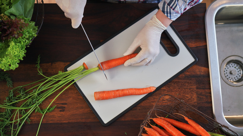 Hands cutting carrots on plastic board