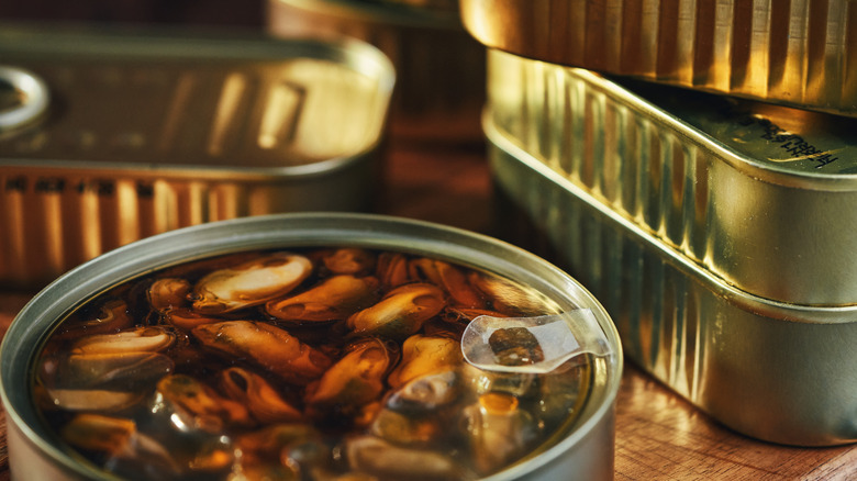 can of mussels in brine next to stacked tins of fish