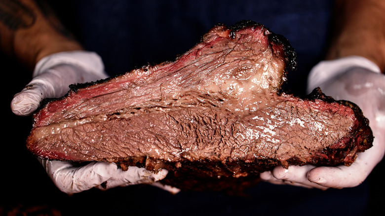 Hands holding smoked brisket 