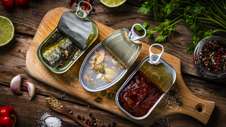 Canned seafood on wooden board; ingredients surrounding them