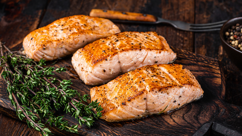 three cooked salmon filets on a board with herbs