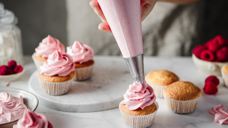 Person piping pink frosting on cupcakes