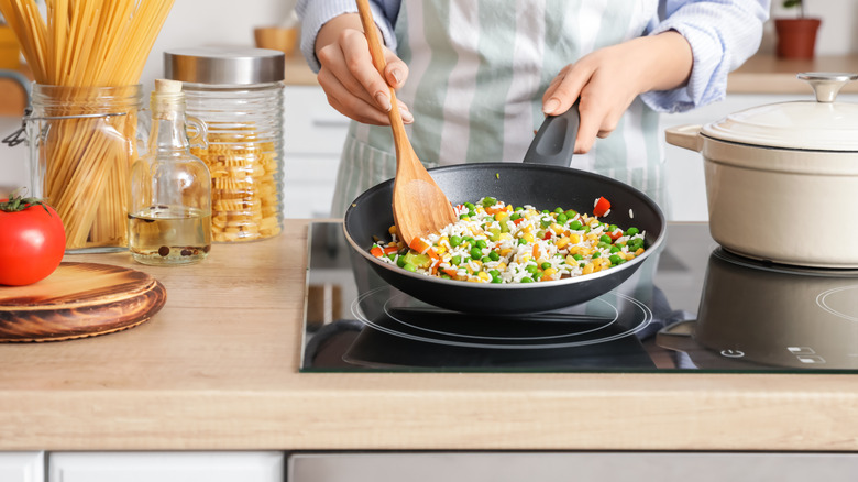 vegetables being cooked in a frying pan with a wooden spoon 