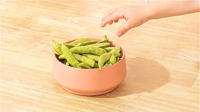 Child hand reaching for green vegetables in bowl