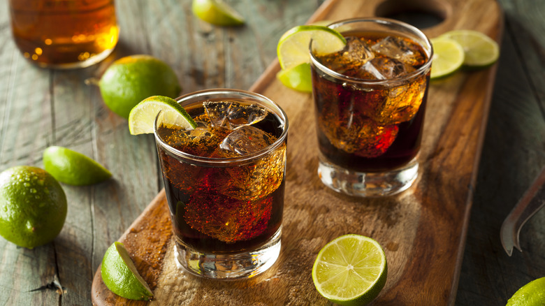 Cuba Libre cocktails with lime wedges on a wooden serving board