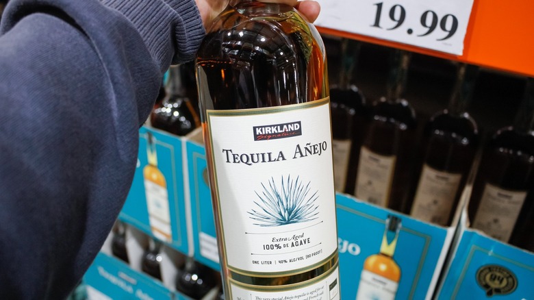 hand holding a bottle of Kirkland Signature Añejo Tequila