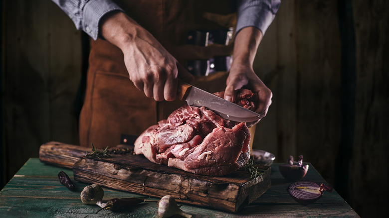 Man wearing apron cutting beef