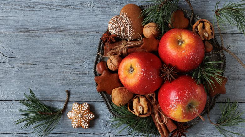 An intricately decorated rustic plate with apples, walnuts, rosemary and star anise.