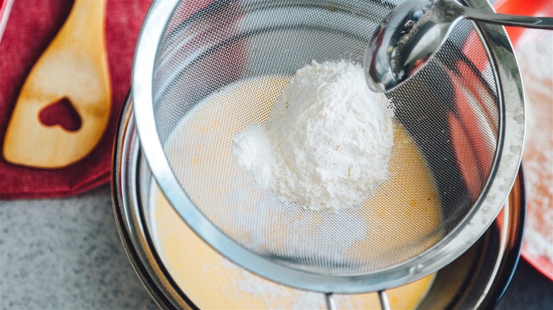 Person sifting flour over bowl