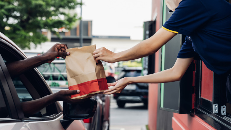 A drive-thru worker handing a driver in their car a bag of food.