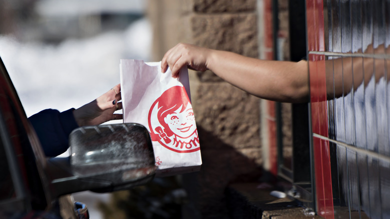 Handing Wendy's bag to customer at drive-thru