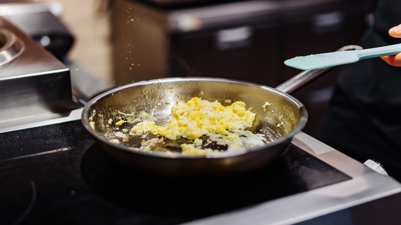 person scrambling eggs on stove