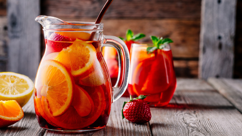 A pitcher of sangria on a table with glasses and cut fruit