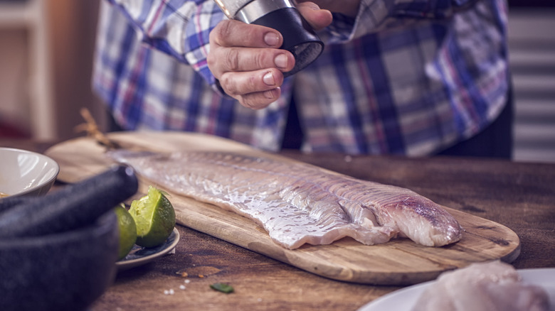 Person sprinkling salt on flounder