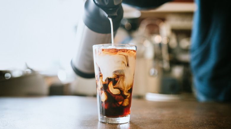 cream being poured into a glass of iced coffee