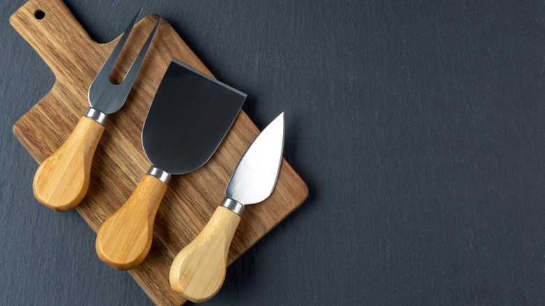 three cheese knives on wooden board