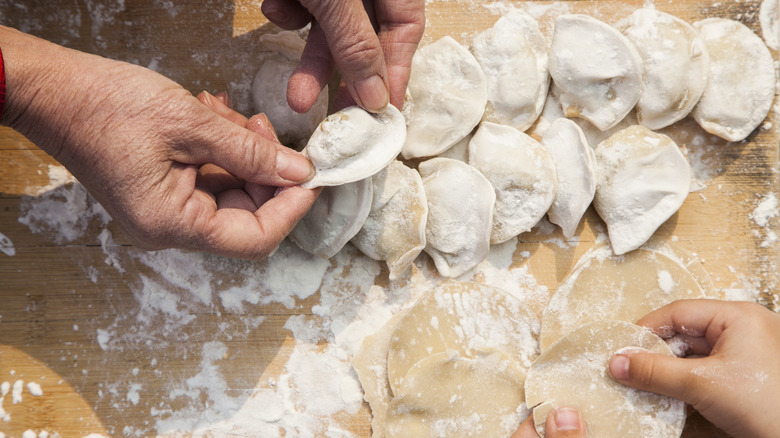 People making jiaozi on a floured worktop