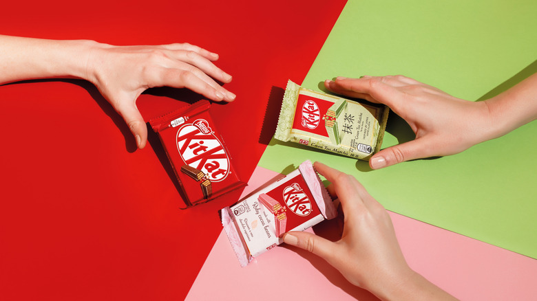 three arms reaching for three different flavors of Japanese Kit Kats