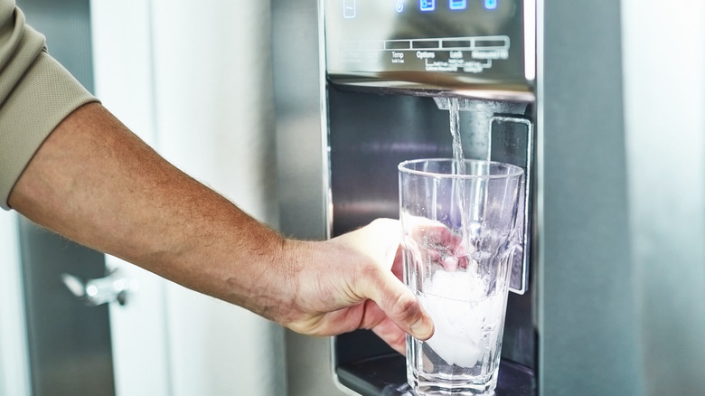 Man filling glass with water from refrigerator door