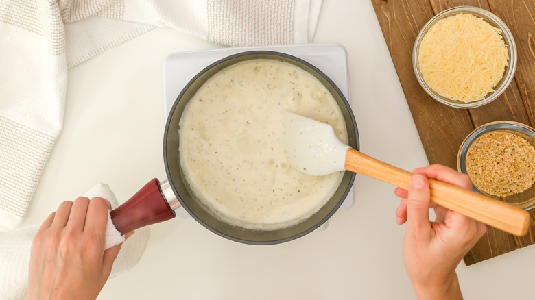 chef's hands mixing Alfredo sauce