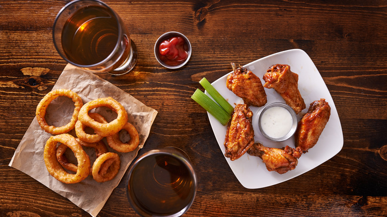 Onion rings, buffalo wings, and two beers on wooden table