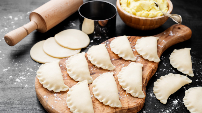 uncooked pierogi on cutting board near bowl of potato filling