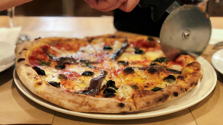 hand cutting anchovy pizza