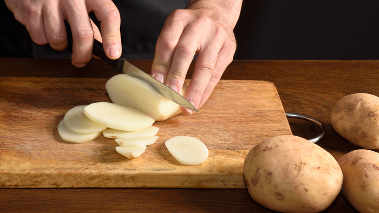 Person slicing potatoes on board