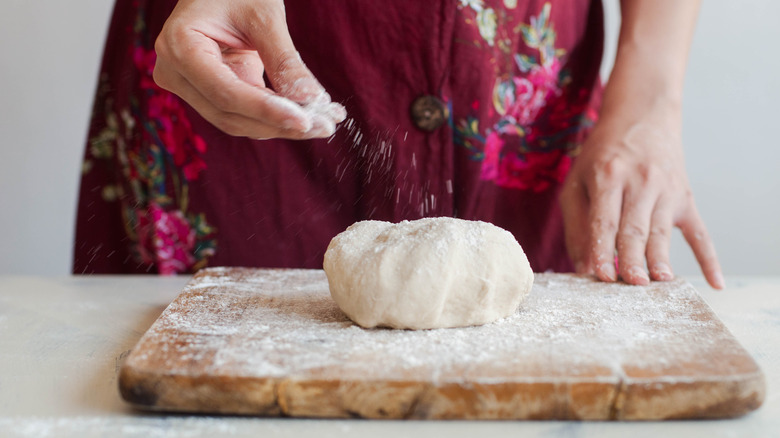 person sprinkling flour on dough