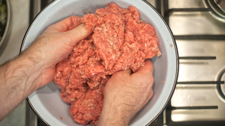 Hands mixing meatballs in white bowl